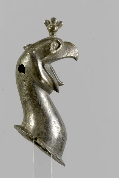 Greifenprotome, gegossen, sehr dickwandig, reduziert, Loch am Hinterkopf, Ansatzring fragmentiert, beide Ohren verloren, Augen waren flach eingelegt, blütenförmiger Knauf, Kernmasse entfernt