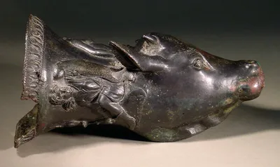 Stierkopfrhyton (Rhyton, Rhyton. Trinkhorn in Form eines Rinderkopfes, Reliefdarstellung mit einer Szene von drei plastischen Figuren; größeres Stück am Rand weggebrochen)