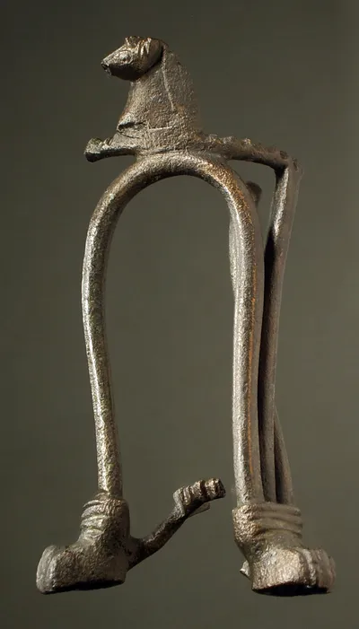 Fragment eines Miniaturdreifußes (Stabdreifußes), leicht verbogen, erhalten zwei Löwenfüße mit Gestänge, Rest des unteren Ringes, des oberen Ringes mit Pferdeprotome, reduziert