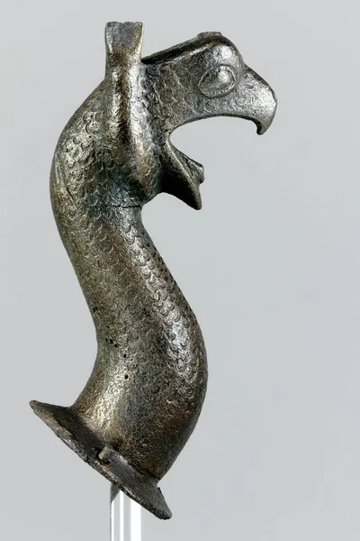 Greifenprotome, gegossen, reduziert, Oberfläche stark angegriffen, Gussfehler am Hals unten, Knauf verloren, Ohren fragmentiert