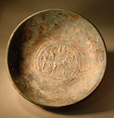 Bronzeschale (Schale einer Griffschale (Ansatzspur des verlorenen Griffs deutlich erkennbar) mit Reliefmedaillon: Krieger auf sprengendem Gespann gegen eine Stadtmauer andringend, auf der zwei Gegner erscheinen)