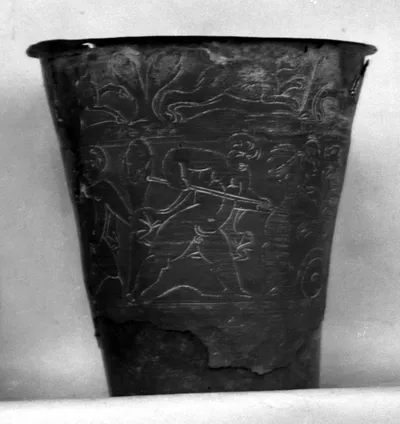 Fragmentierter spätantiker Becher (genauer: ein kleiner Eimer) mit drei Friesen gravierter und teilweise mit Weissmetall überzogener Zeichnungen: oben und unten Rehe und Hasen jagende Hunde; im mittleren Streifen Eroten im Kampf mit Tieren